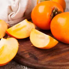 Saftige, leuchtend orangefarbene Persimmon-Früchte, einige ganz, andere in Spalten geschnitten, liegen auf einem Holzbrett.