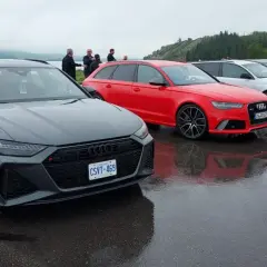 Szare i czerwone Audi RS6 C8 stoją obok siebie na mokrym parkingu.
