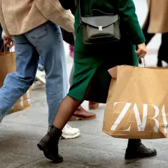 Ludzie idący ulicą z torbami na zakupy. Jedna z toreb ma wyraźne logo ZARA, sugerując udany zwrot lub zakupy w tym sklepie.
