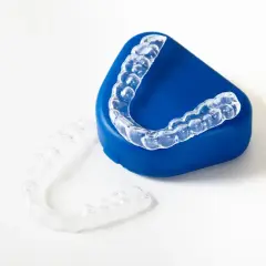 Alineadores transparentes para ortodoncia, uno sobre un estuche azul y otro al lado. ¿Cuánto cuesta el invisible line?