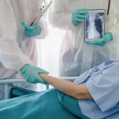 Lekarze w kombinezonach ochronnych trzymają tablet z rentgenem płuc pacjentki. Dają jej nadzieję na powrót do zdrowia, być może dzięki leczeniu remdesivirem.