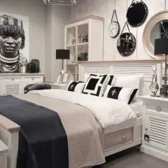 Sypialnia boho loft z łóżkiem, czarnymi lampami i portretem kobiety. Dekoracje ścienne dodają charakteru.
