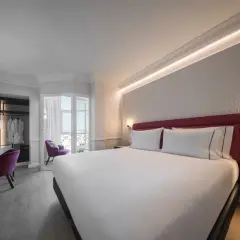Habitación moderna y luminosa en el hotel San Antón Granada. Cama doble con cabecero rojo, escritorio, sillón morado y vistas.
