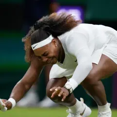 Serena Williams upada na kort podczas meczu tenisa w Wimbledonie, trzymając rakietę.