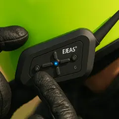 Mano con guante negro ajustando un intercomunicador moto homologado DGT en casco verde.
