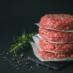Stos surowych kotletów na burgery, idealne mięso na burgery, z gałązką rozmarynu i pieprzem w tle.