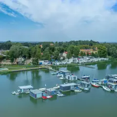 Nowoczesne houseboat'y unoszą się na spokojnej wodzie, obok kempingu z kamperami.