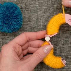 Hände wickeln gelbes Garn um eine Pompon-Schablone. Tolle Pompon-Ideen für dein nächstes Projekt!
