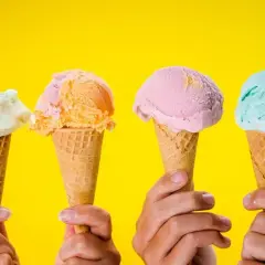 Vier Hände halten bunte Speiseeis-Sorten in Waffeln vor gelbem Hintergrund.