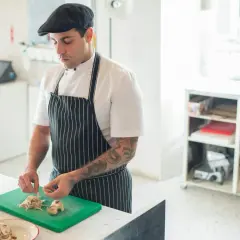 Chef con gorra y delantal a rayas, cortando champiñones en una tabla verde. Ideal para aprender a cocinar.