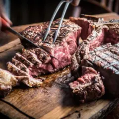 Una succulenta fiorentina steak, tagliata al sangue su un tagliere di legno rustico, con un coltello che affonda nella carne.