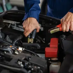 Mekaniker kopplar startkablar för att ladda nytt bilbatteri.