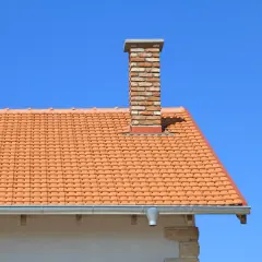 Ceglany komin na dachu z pomarańczowej dachówki. Zastanawiasz się, ile kosztuje budowa komina?