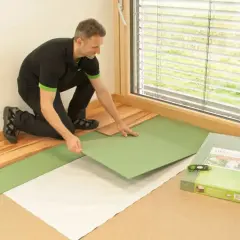 Mężczyzna układa zieloną podłogę, która jest podkładem pod panele z ogrzewaniem podłogowym.