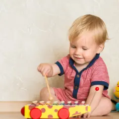 Roczniak bawi się cymbałkami, otoczony kolorowymi zabawkami. To idealne kreatywne zabawy dla rocznego dziecka, rozwijające jego zmysły i koordynację.