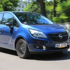 Niebieski Opel Meriva 1.4 benzyna w ruchu miejskim, z rozmazanym tłem drzew i budynków.
