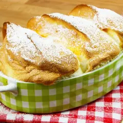Ein goldbrauner, luftiger Salzburger Nockerl-Auflauf, bestäubt mit Puderzucker, in einer grünen Karamikform.