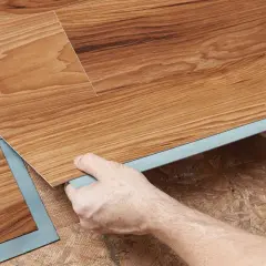 Hands installing wood-look vinyl plank flooring. Once installed, you can walk on vinyl plank flooring immediately.