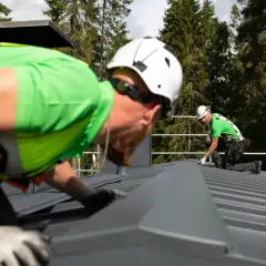Två takläggare i varselkläder arbetar på ett tak. De är på väg att laga papptaket.