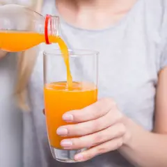 Kobieta nalewa sok pomarańczowy do szklanki. Może to być część diety, gdy triglicerydy za wysokie.