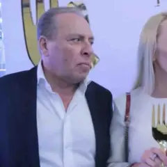 Wojtek Kurowski, wiek nieznany, w garniturze i białej koszuli, obok kobiety z złotym trofeum w kształcie dłoni.