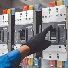 Ręka w czarnej rękawiczce obsługuje wyłącznik rozłącznik odłącznik w panelu elektrycznym.