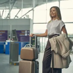 Elegancka kobieta w stylowym ubraniu do samolotu, z walizkami i płaszczem, czeka na lotnisku.