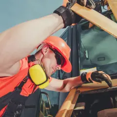 Operator w kasku i ochronnikach słuchu sprawdza silnik koparki.