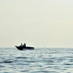 Due persone su un'imbarcazione con potenti motori marini navigano su un mare calmo, lasciando una scia d'acqua.
