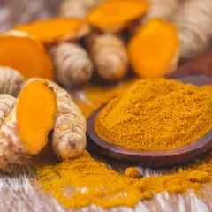 Radici di curcuma fresche e in polvere, un elemento chiave nell'elenco spezie indiane, su un cucchiaio di legno.