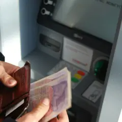 Ręka trzyma portfel z kartami i banknotami przy bankomacie. Sprawdzam saldo i dostępne środki przed wypłatą.