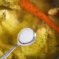 Łyżeczka soli czeka na dodanie do bulionu z kurczakiem i marchewką. Idealny moment, kiedy solić rosół, by wydobyć pełnię smaku.
