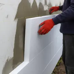 Pracownik w czerwonych rękawicach montuje płyty styropianowe do ściany. Sprawdź ocieplenie elewacji cena.