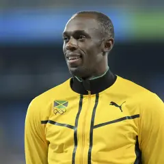 Usain Bolt w żółtej kurtce z flagą Jamajki i logo olimpijskim. Zastanawiasz się, jak szybko biega Usain Bolt?