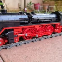 Detailreiche Lego Dampflok MOC mit roten Rädern und schwarzem Gehäuse auf Schienen.