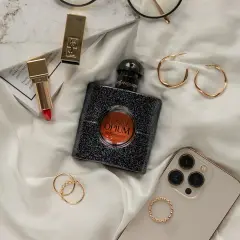 Elegancka kompozycja z flakonem perfum **black opium**, złotą szminką, pierścionkami i telefonem.