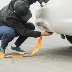 Mężczyzna mocuje pomarańczową linę holowniczą do samochodu. Pamiętaj o ograniczeniach prędkości podczas holowania, by zapewnić bezpieczeństwo.