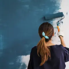 Mujer aplicando imprimación azul en pared con rodillo. Aprende como dar imprimación en paredes para un acabado perfecto.