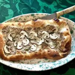 En gyllene pinsa med svamp och örter, redo att skäras med en kniv. Ett perfekt pinsa recept för en mysig kväll.