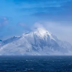 Majestuosa montaña nevada emerge de las aguas agitadas, un paisaje que evoca el temido paso de Drake.