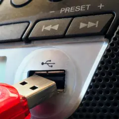 Czerwony pendrive podłączony do portu USB urządzenia. Widoczne przyciski sterowania i głośnik. Parowanie danych z pamięci przenośnej.