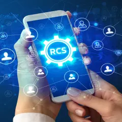 Dłonie trzymają smartfon z ikoną RCS w centrum, otoczoną siecią połączeń i symboli użytkowników na tle danych.