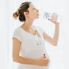 Une femme enceinte boit de l'eau d'une bouteille, prenant soin de son hydratation.