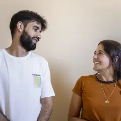 Un baldo giovane con barba e una donna sorridono guardandosi. Lui indossa una maglietta bianca con la scritta "Positive".