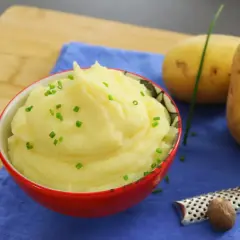 Un cremoso puré de patatas, adornado con cebollino fresco, junto a patatas crudas y una nuez moscada.