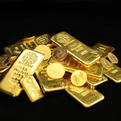 Złote sztabki i monety, w tym słynny Krugerrand, błyszczą na czarnym tle.