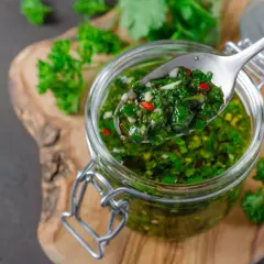 Łyżka z aromatycznym chimichurri, pełnym ziół i chili, nad słoikiem pełnym tej zielonej, pysznej pasty.