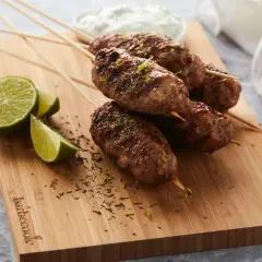 Brochettes d'agneau grillées, garnies d'herbes et de zeste de citron vert, servies avec des quartiers de citron vert et une sauce blanche.