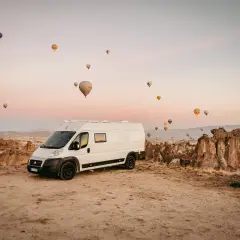 Kamper na tle skalistego krajobrazu Kapadocji, gdzie w powietrzu unoszą się liczne balony. Niezwykłe widoki, jak z innych turcja miasta.