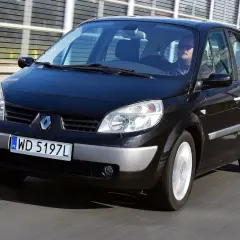 Czarny Renault Scenic 2 jedzie po drodze. Kierowca w okularach przeciwsłonecznych prowadzi auto.